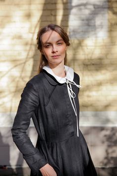 a woman standing in front of a building wearing a black dress and white collared shirt