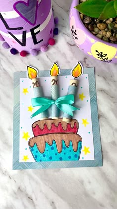 a birthday card with candles on it and a potted plant next to it in the background