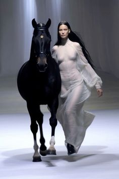 a woman walking next to a black horse on a runway