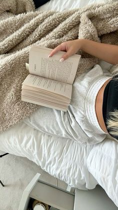 a woman laying in bed with an open book on top of her head and two candles beside her