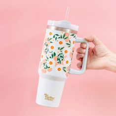 a hand holding a coffee cup with flowers on the side and a straw in it