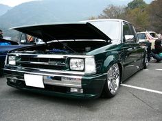 a green car with its hood open parked in a parking lot next to other cars