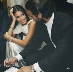 a man and woman sitting next to each other in front of a table with papers