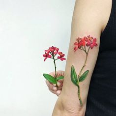 a woman with a flower tattoo on her arm holding a red and white flower in one hand