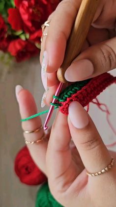 a woman is crocheting the end of a piece of red and green yarn