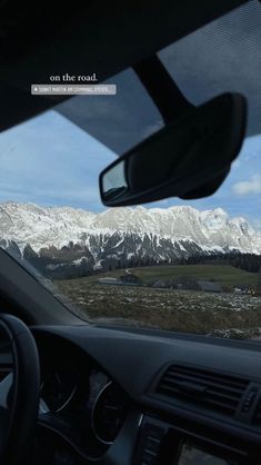 the view from inside a car looking at mountains and snow capped peaks in the distance