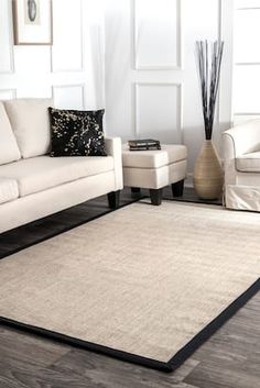 a living room with white couches and black trimming on the rug, along with two chairs