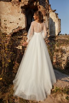 a woman standing in front of an old building wearing a wedding dress with long sleeves