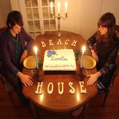 two people sitting at a table with a cake in front of them that says beach house