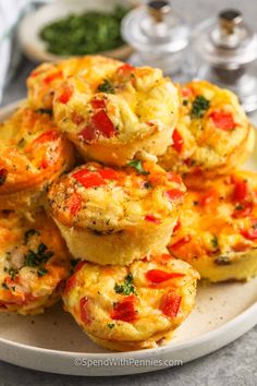 small muffins with tomatoes and herbs on a white plate next to other food items