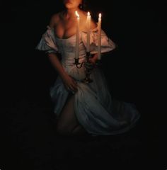 a woman sitting in the dark holding three candles