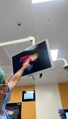 a man in scrubs is operating a large screen monitor on the ceiling above his head