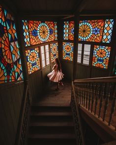 a girl in a white dress is walking down the stairs with stained glass windows behind her