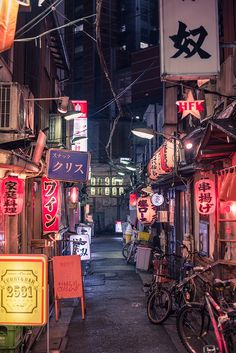 an alley way with many signs and bicycles parked on the side of it at night