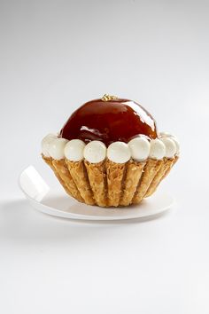 a cupcake on a white plate topped with whipped cream and cherry sauce, sitting on a white surface