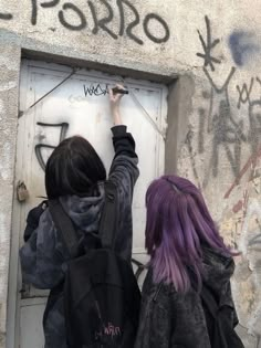 two people writing on a wall with graffiti