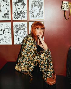 a woman sitting on top of a wooden table in front of some art work hanging on the wall