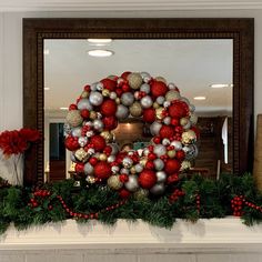 a christmas wreath is displayed in front of a fireplace with red and silver ornaments on it