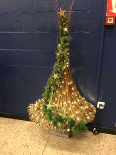 a christmas tree made out of branches with lights on it in front of a blue wall