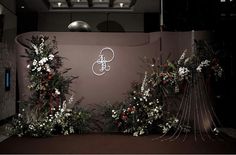 the wall is decorated with flowers and greenery in front of an illuminated sign that reads,