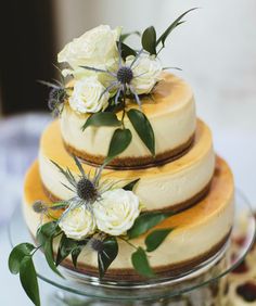 a three tiered cake with white flowers on top and greenery around the edges