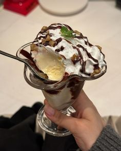 a person holding an ice cream sundae with chocolate sauce and walnuts on top