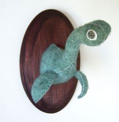 a small stuffed animal sitting on top of a wooden plaque with a button in the shape of a lizard