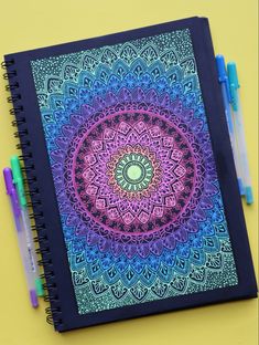 a notebook with an intricate design on the cover and two markers next to it,