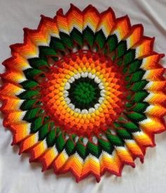 an orange and green crochet doily on a white sheet with the center surrounded by leaves