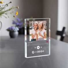 a glass photo frame sitting on top of a table next to a vase with flowers