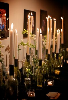 candles are lit in front of bottles with flowers and greenery on the table next to them