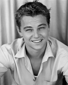 a black and white photo of a man with short hair smiling at the camera, wearing a button up shirt