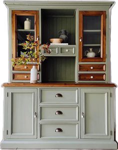 an old china cabinet painted green with wood trimmings and flowers in vase on top