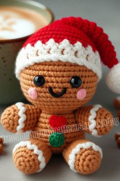 a crocheted teddy bear with a red and white hat sitting next to a cup of coffee