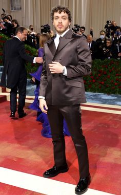 a man in a tuxedo standing on a red carpet with cameras around him