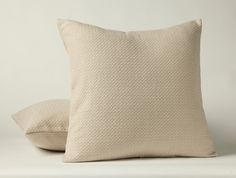 two pillows sitting next to each other on top of a white surface with a light colored background