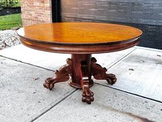 a wooden table sitting on top of a sidewalk next to a brick building and grass