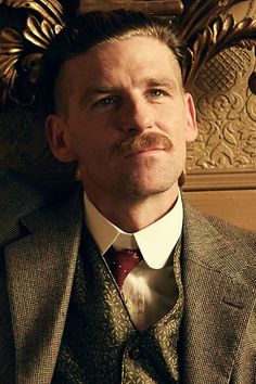 a man wearing a suit and tie in front of a wall with gold decorations on it