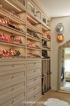 a closet with many pairs of shoes on shelves and a large mirror in the corner