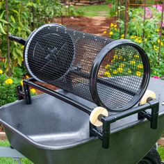 an outdoor grill with two fans on the top and wheels, in front of some flowers