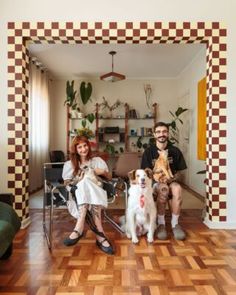 two people sitting on chairs with dogs in front of them and the dog is looking at the camera