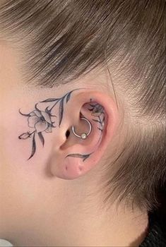 a woman with tattoos on her ear and behind the ear is a small flower tattoo