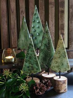 three green trees sitting on top of a table next to some pine cones and candles