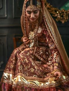 a woman in a red and gold wedding dress sitting on a chair with her head down