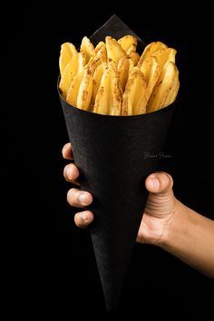 a hand holding a cone of fries in it's left hand, on a black background