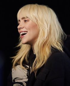 a woman with blonde hair smiling and looking to the side while wearing a black jacket