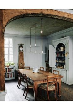 an old fashioned dining room table with chairs and a grandfather clock on the wall behind it