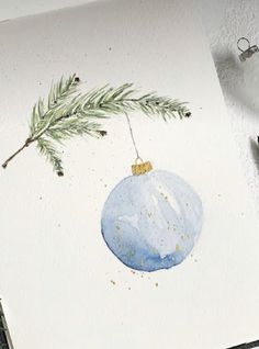 a watercolor painting of a blue ornament hanging from a pine tree branch