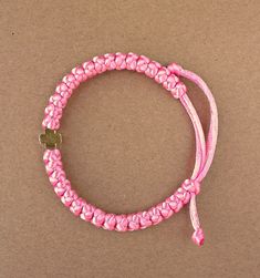 a pink bracelet with a gold heart charm on the end and a cord attached to it