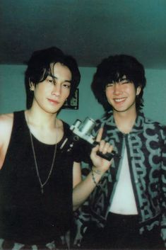 two young men standing next to each other holding an object in one hand and a camera in the other